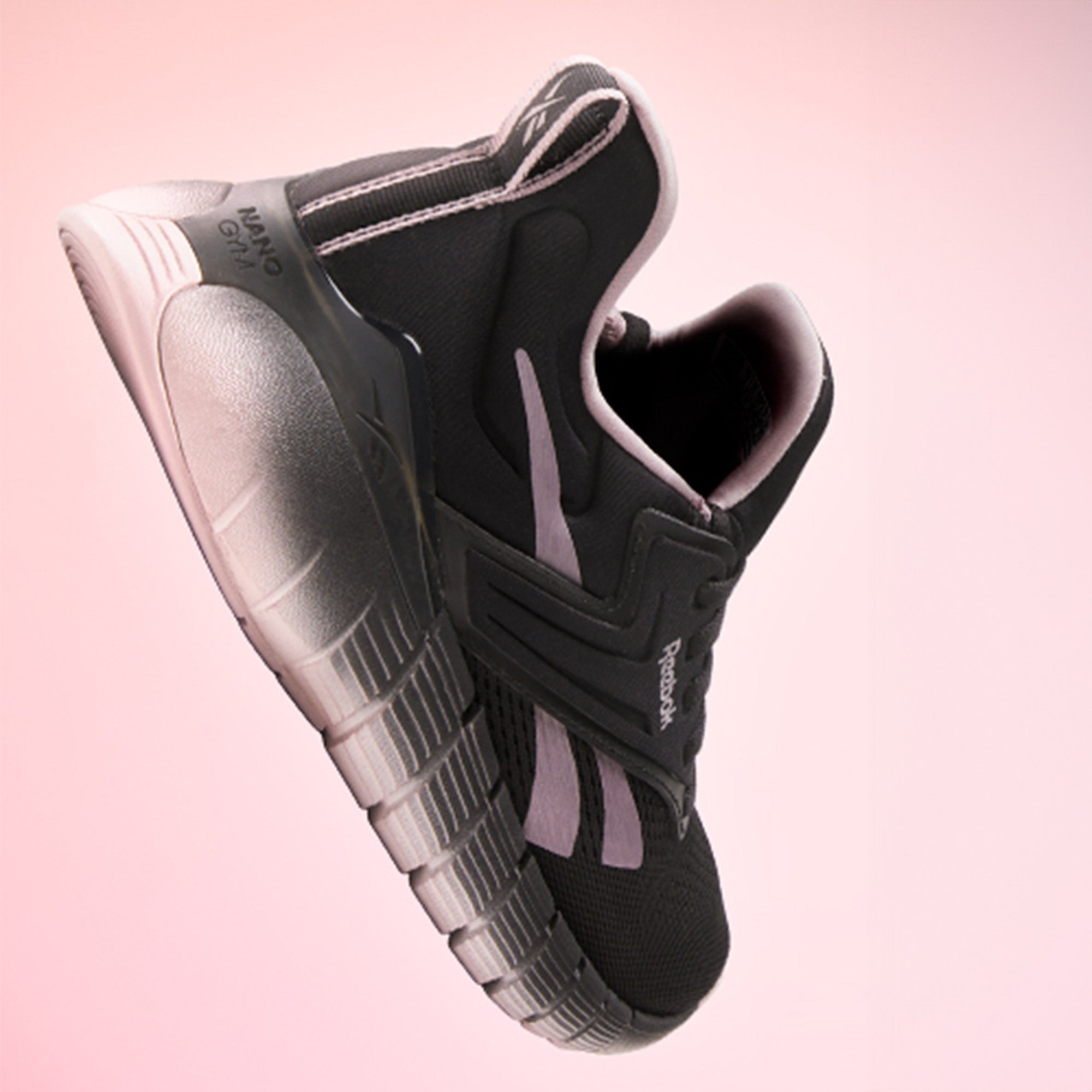 A pair of Reebok Women's Nano Gym Training Shoes in black with white soles and pink accents, shown from above on a white background. Versatile for workouts, they feature the Reebok logo on the insoles.