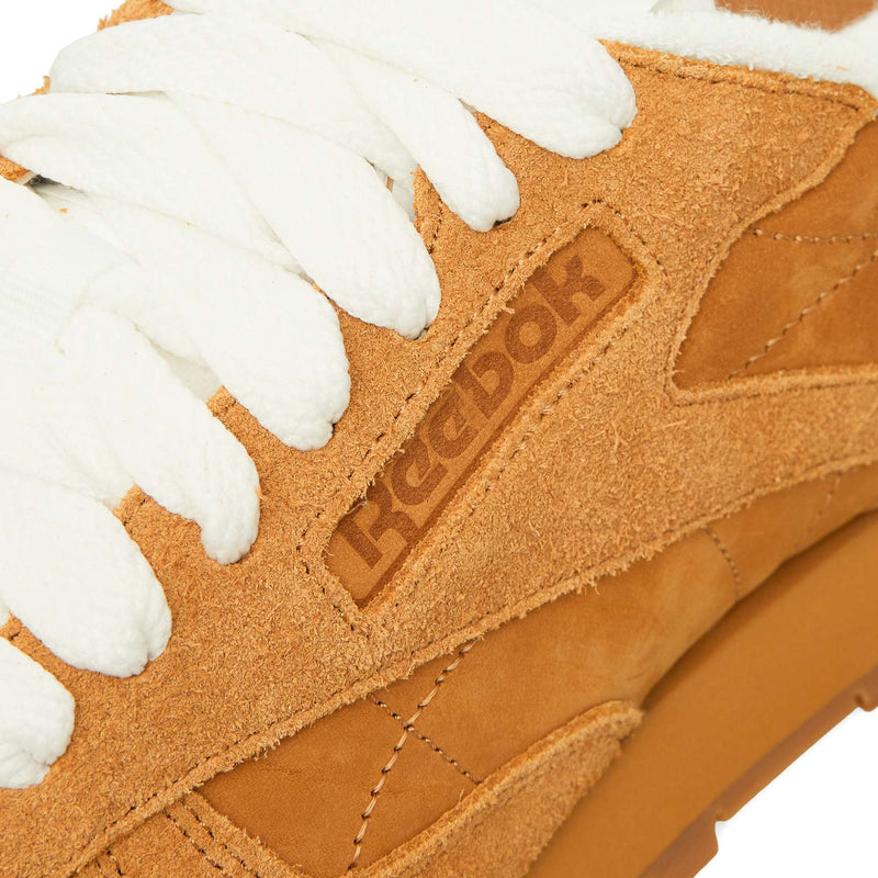 Close-up of a tan suede Reebok Classic Leather Premium sneaker with white laces, showcasing its timeless silhouette.