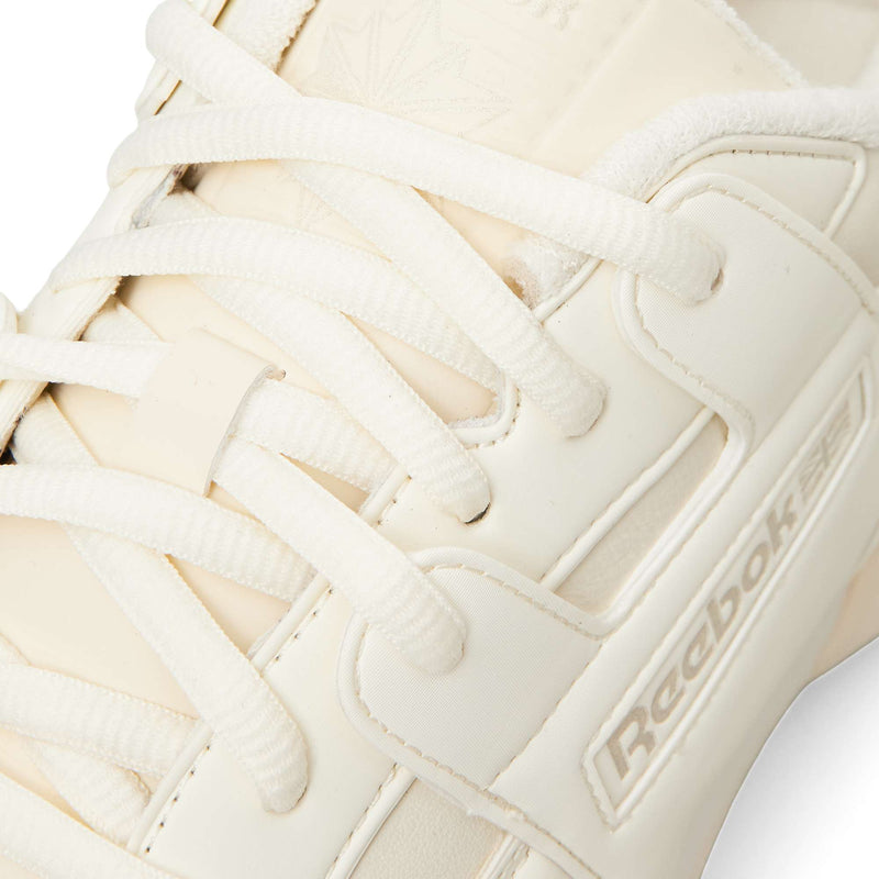 Close-up of a cream-colored Reebok Workout Plus OG sneaker, featuring a classic silhouette with matching flat laces and embossed branding on the side panel.