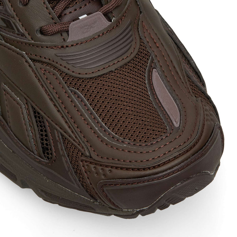 Close-up of a dark brown Reebok Premier Road Ultra running sneaker, featuring a mesh toe box and layered synthetic overlays atop a dual-density midsole.