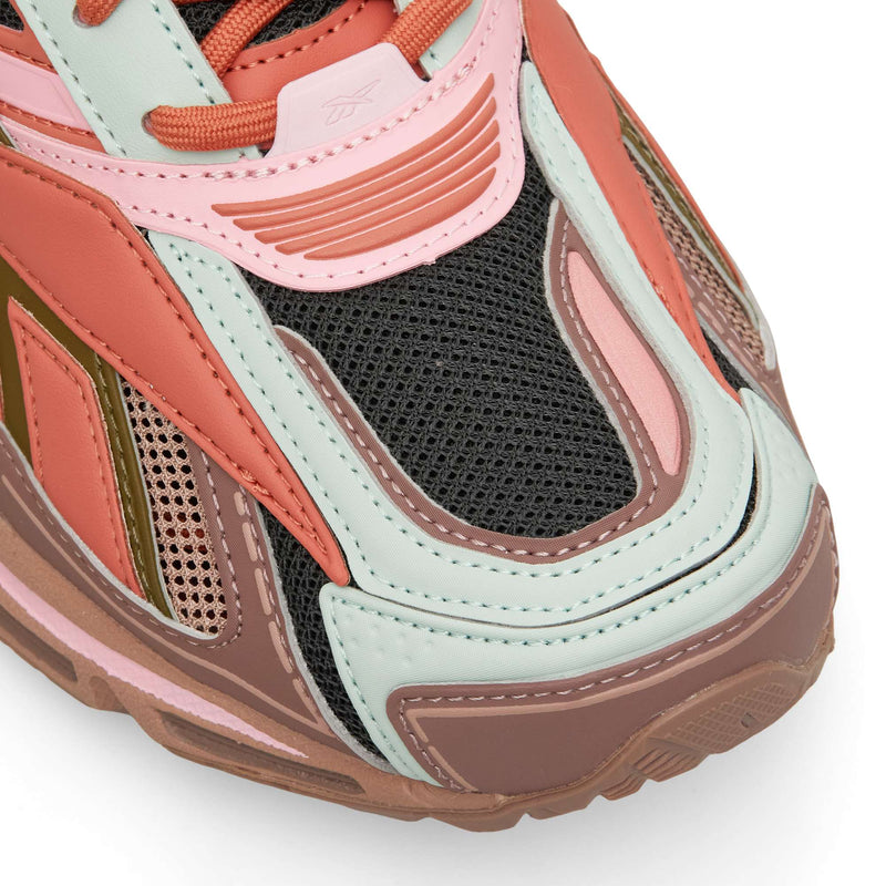 Close-up of a Reebok Premier Road Ultra athletic shoe in shades of pink, mint green, and dark brown, featuring mesh panels and textured overlays on a dual-density midsole.