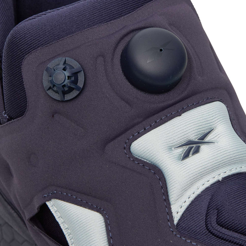 Close-up of a dark-toned Reebok Instapump Sliver slip-on sneaker featuring a circular pump mechanism on the tongue and a branded tab on the upper.