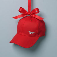 A red Reebok baseball cap hanging from a red ribbon bow against a light gray background.