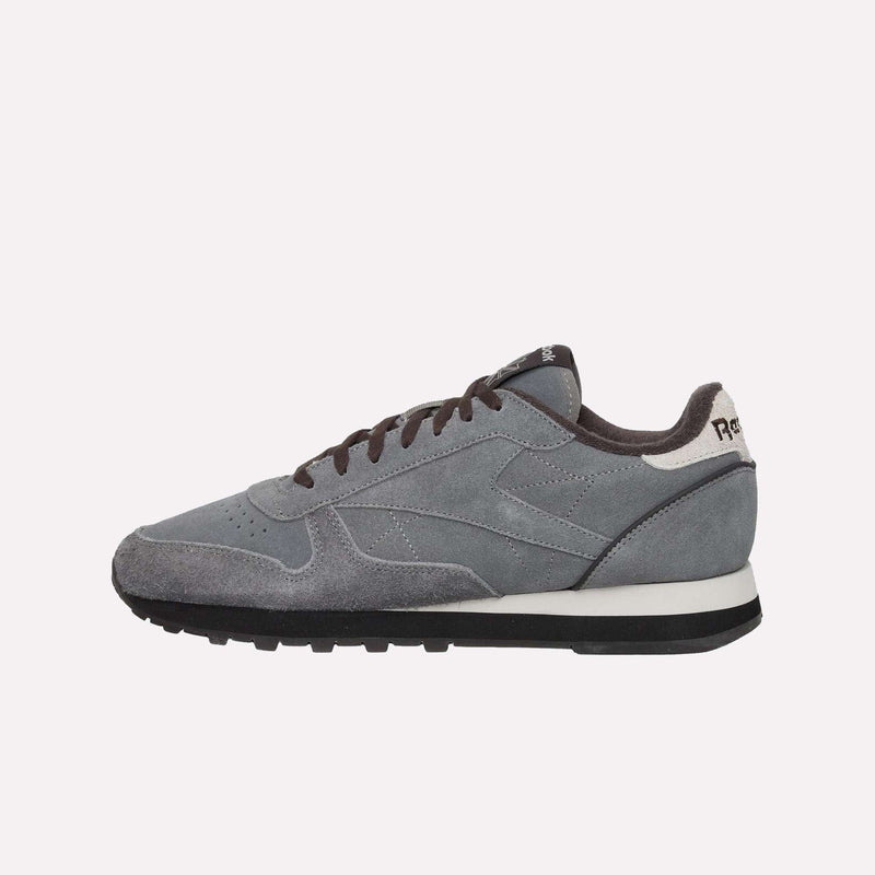 A gray and black sneaker with white accents features a suede upper, black laces, and a black rubber sole. Showcasing a classic silhouette reminiscent of retro sneakers, the Reebok Classic Leather Premium LTD Shoes are displayed in side profile against a plain, light background.