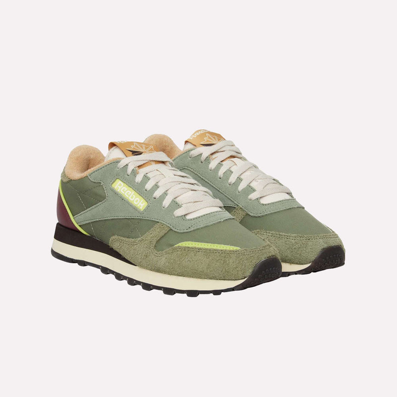 A pair of Reebok Classic Leather Premium LTD Shoes in green, featuring beige laces, yellow and maroon accents, and a textured sole, displayed against a plain white background. These sneakers boast a classic silhouette that exudes retro charm.
