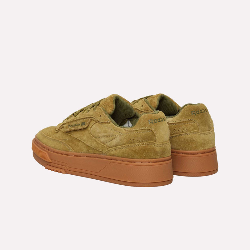 A pair of Reebok Club C LTD Shoes in tan suede, featuring brown rubber soles and displayed at an angle on a plain white background, embody the effortless style of a classic lifestyle tennis sneaker.