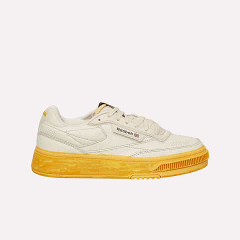 The Reebok Club C LTD Shoes in beige feature a textured leather upper and a bold, bright yellow sole, showcased in a side profile view against a plain white background—a modern take on the timeless tennis-inspired classic.