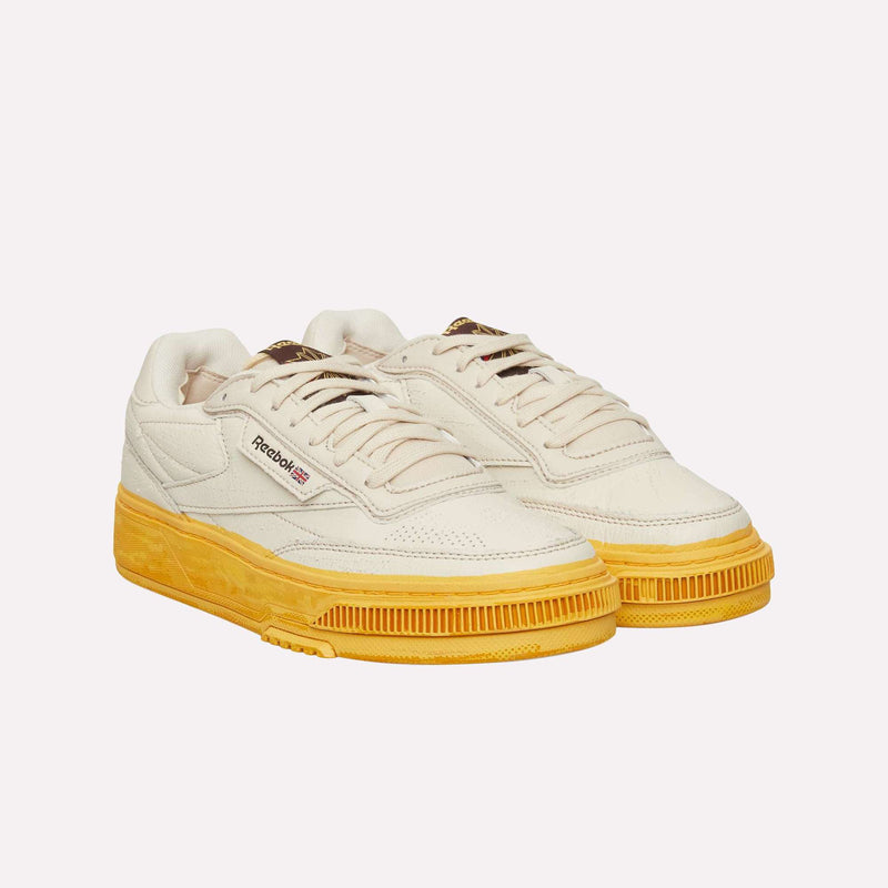 A pair of Reebok Club C LTD Shoes in off-white, featuring thick, textured yellow soles, displayed at an angle against a plain white background—a timeless lifestyle classic.