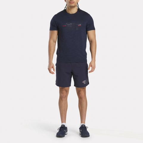 A man faces forward against a white background, wearing the Reebok Men's Core Training Kit with a performance shirt, matching navy athletic shorts, white socks, and navy training shoes.