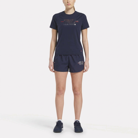 A woman faces forward in the Reebok Women's Core Training Kit—navy athletic t-shirt, shorts, and sneakers—modeling stylish workout wear against a plain white background.