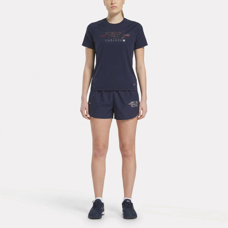 A woman faces forward in the Reebok Women's Core Training Kit—navy athletic t-shirt, shorts, and sneakers—modeling stylish workout wear against a plain white background.