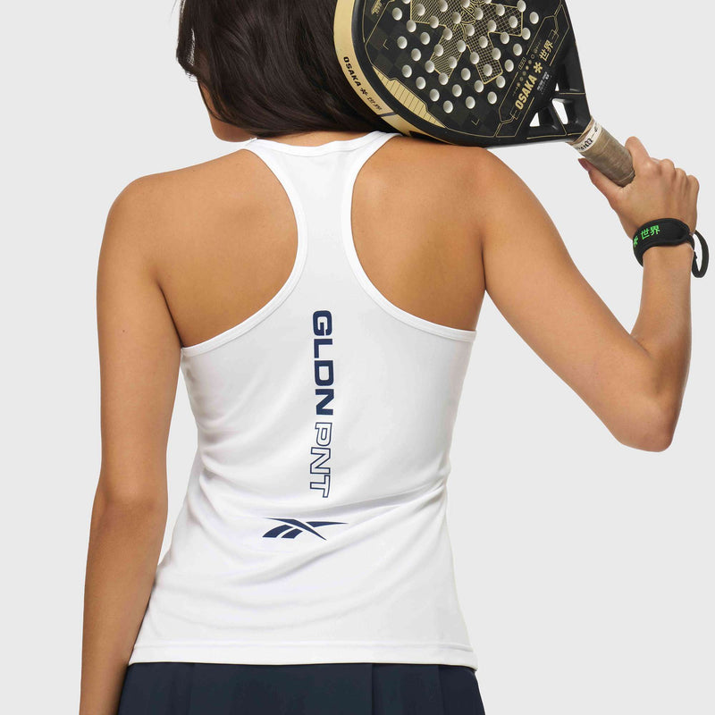 A woman seen from behind holds a padel racket over her shoulder. She wears a white Reebok x GLDN PNT Women’s Tank Top with “GLDN PNT” and logo on the back, a black skirt, and a black wristband with green text.