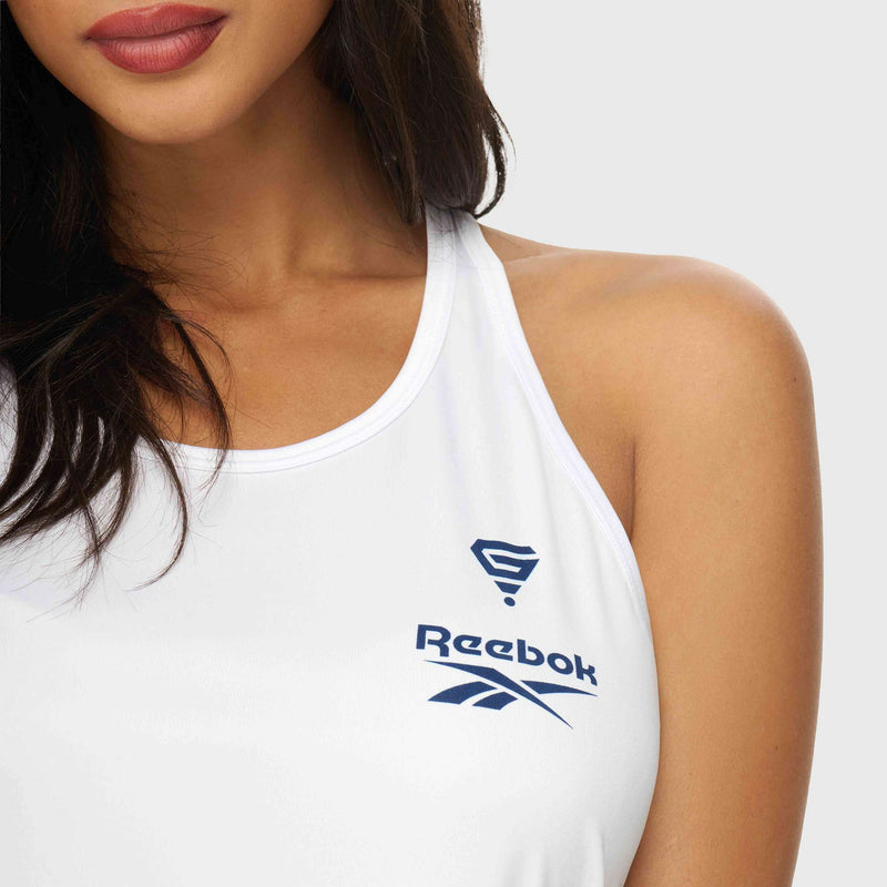 A woman wears the Reebok x GLDN PNT Women’s Tank Top in white, featuring blue logos. Shown from the shoulders up against a plain light background, her face is partially visible with focus on her lips and chin.
