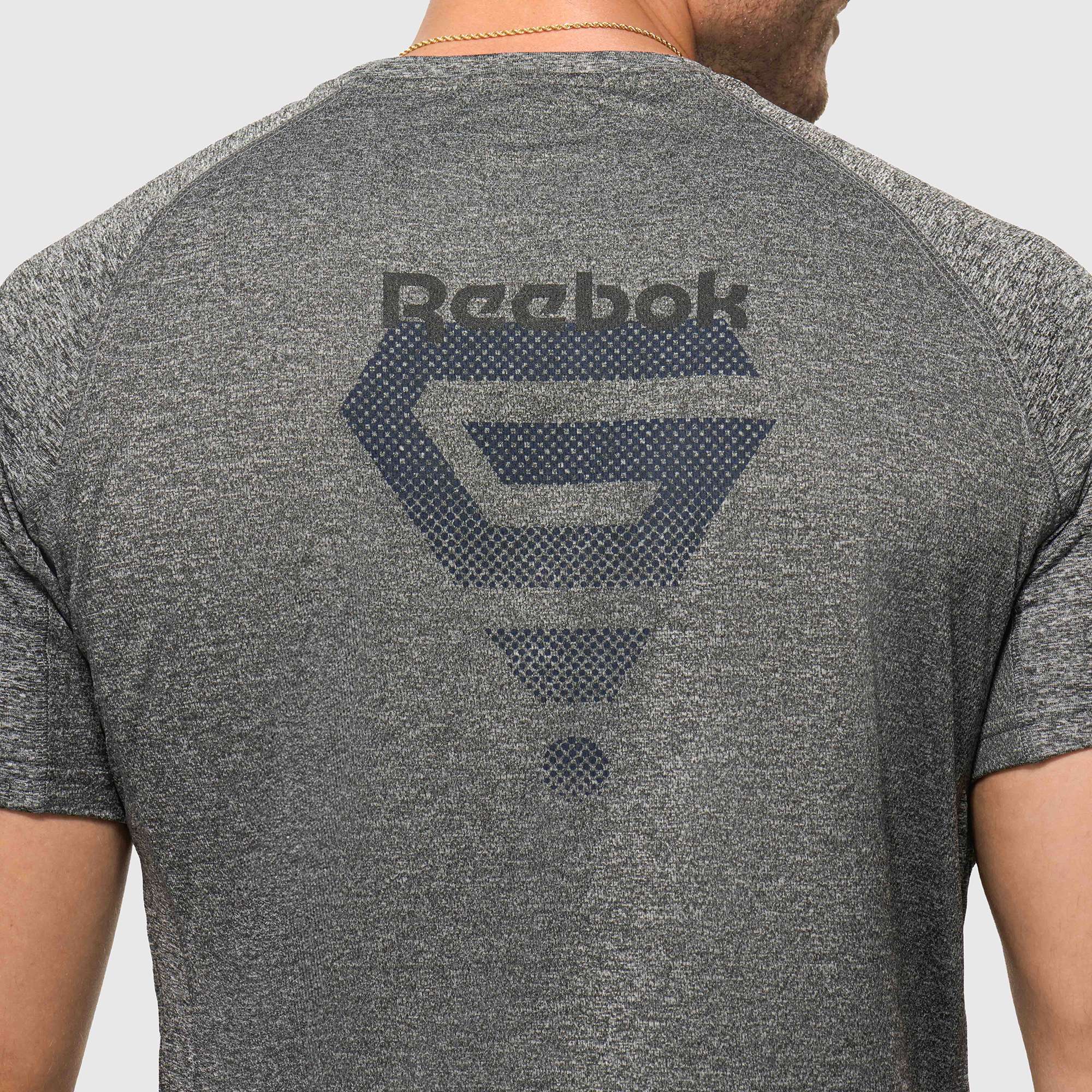 A person is shown from the back wearing a lightweight Reebok x GLDN PNT Tech Tee in heather gray, featuring a large dark Reebok logo and graphic design across the upper back.