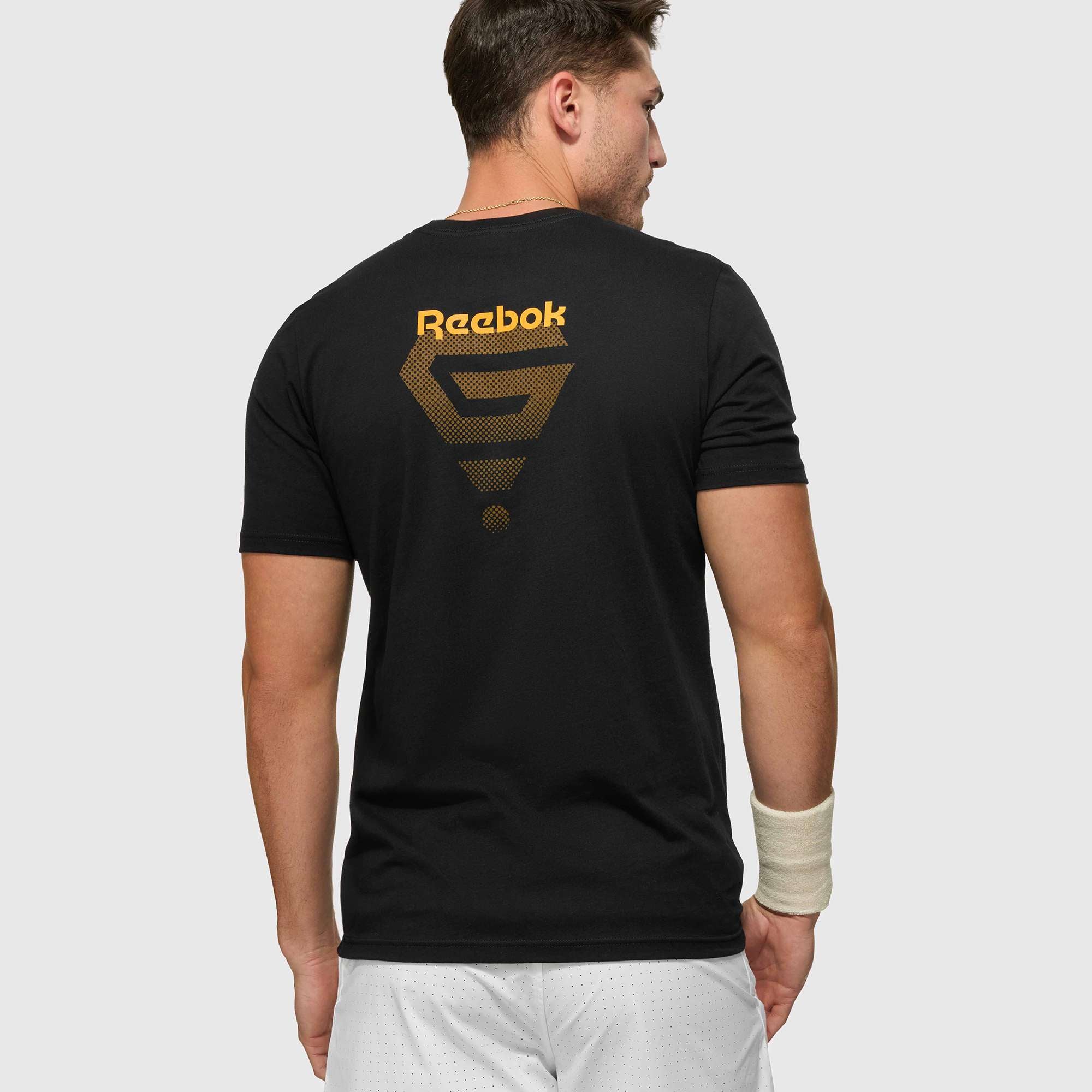 A man wears the Reebok x GLDN PNT Jersey Tee, a black premium cotton t-shirt by Reebok featuring a bold gold logo and back design. He pairs it with a white wristband and shorts against a plain background.