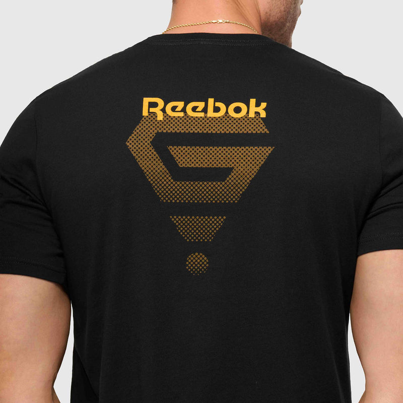 A person wears the Reebok x GLDN PNT Jersey Tee, a premium cotton unisex shirt with a black base, gold Reebok logo, and geometric back design. The image highlights the upper back and neck of this minimalist tee.