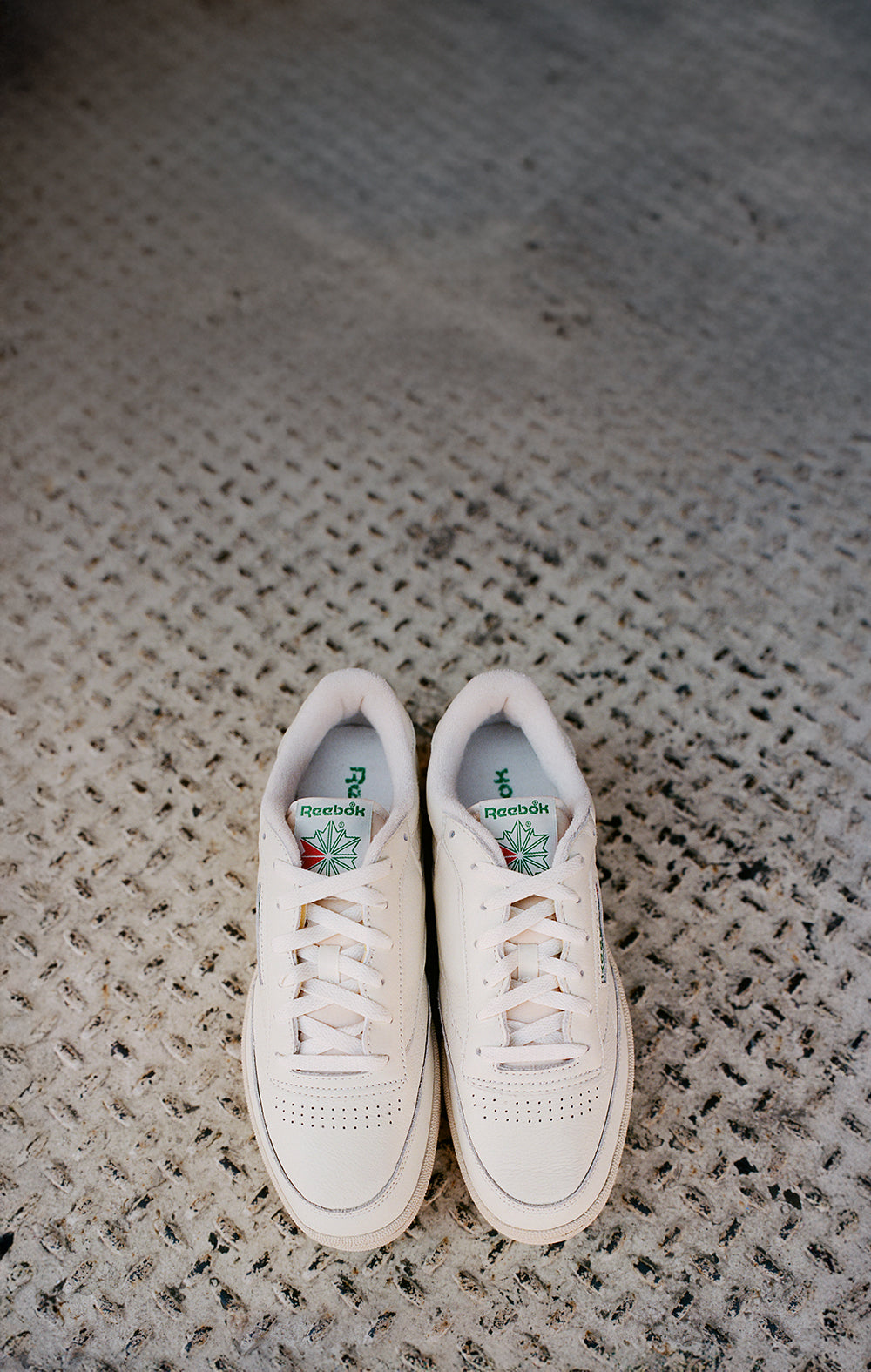 Pair of white sneakers with brand logo on a textured surface
