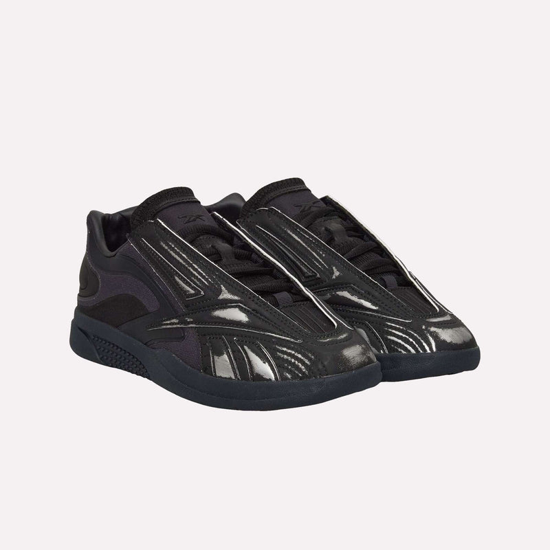 A pair of Hammer Pro LTD Shoes by Reebok in black, featuring silver accents and a sleek, futuristic design. Made from high-quality faux leather with a durable rubber sole, displayed against a plain light background.