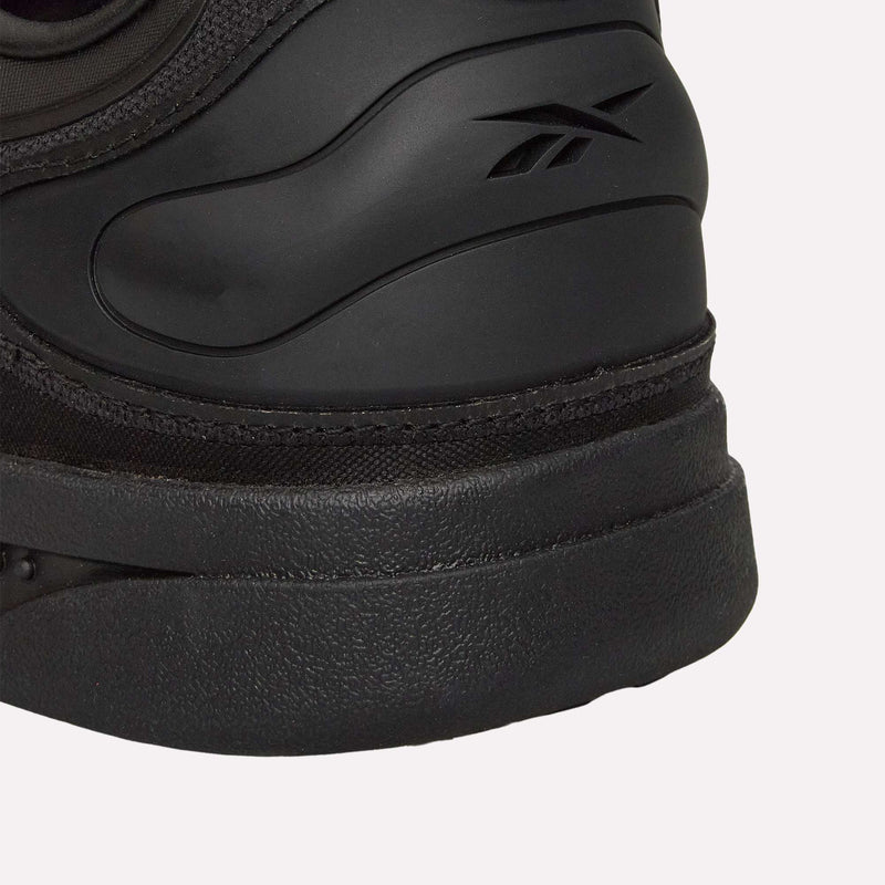 Close-up of the heel of a black Reebok Hammer Pro LTD Shoe, showcasing its textured and durable rubber sole with the Reebok logo embossed on the side. The faux leather upper lends a sleek look, while the plain light background highlights the shoe’s detailed design.