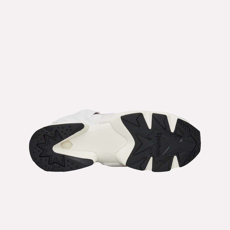 Bottom view of the Reebok Instapump Sliver LTD Shoes in white, highlighting a black rubber outsole with distinct geometric tread patterns and the centrally placed Reebok logo. Equipped with advanced Hexalite cushioning, this model blends superior comfort and performance. The background is plain and light-colored.