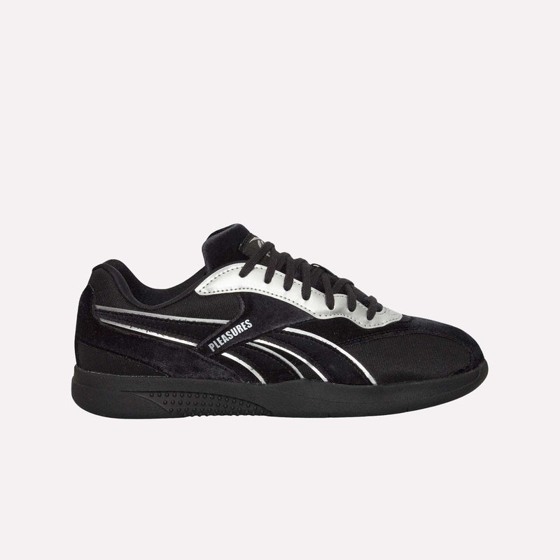 Introducing the Reebok Pleasures Hammer Street Shoes, a striking black sneaker created in collaboration with PLEASURES. This low-top features silver accents and the PLEASURES logo along the side, paired with a sleek black sole and matching laces. The luxurious velvet upper combines premium comfort with sporty style, as showcased against a plain white background.