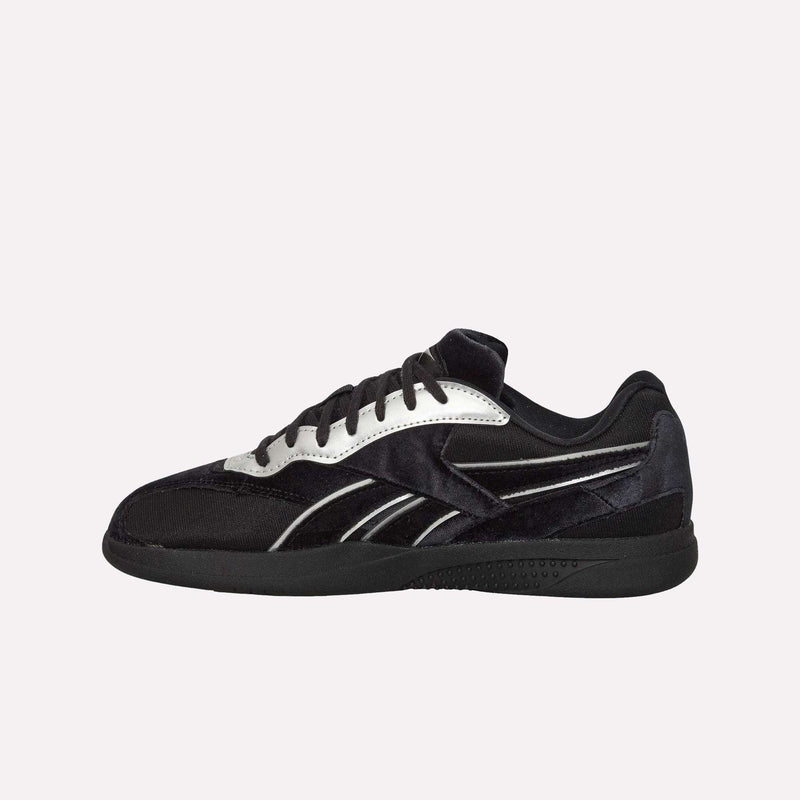The Reebok Pleasures Hammer Street Shoes are black athletic sneakers with white and silver accents, black laces, and a low-cut design—shown in a side profile on a plain white background. They feature a rich velvet upper, blending classic style with modern sophistication.