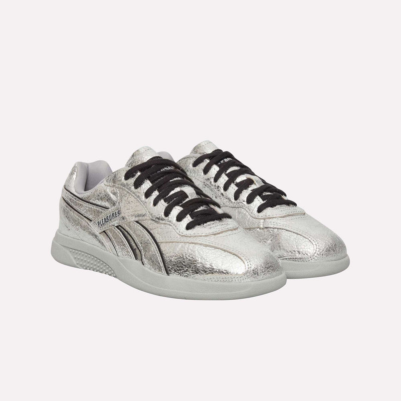A pair of Pleasures Hammer Street Shoes by Reebok, featuring a silver metallic grunge design with black laces and a textured finish, displayed on a white background—an eye-catching piece from their latest collaboration.