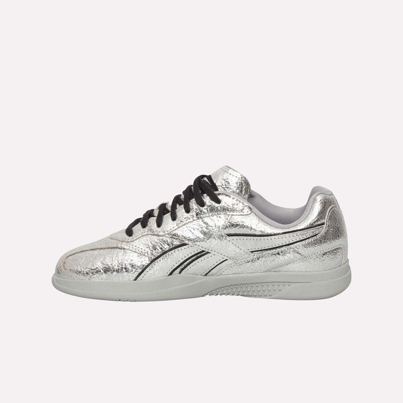 The Reebok Pleasures Hammer Street Shoes—a metallic silver sneaker featuring black laces, black side stripes, and a light gray sole inspired by classic grunge sneakers—are shown against a plain white background.
