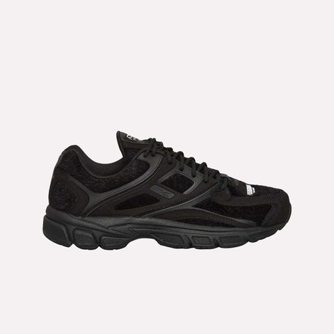 A black athletic sneaker featuring mesh and suede-like panels, black laces, and a chunky black sole, viewed from the side on a plain light background—these standout shoes are the Reebok Pleasures Premier Trinity KFS, a collaboration that merges contemporary style with streetwear influence.