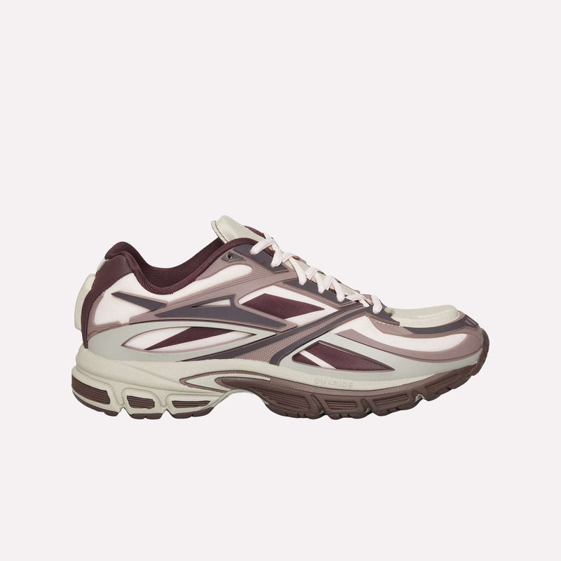 A side view of the Reebok Premier Road Modern LTD Shoes, inspired by archival running shoe aesthetics, showcases maroon, cream, and white accents. The design highlights a layered construction and a thick, patterned sole with a dual-density midsole, set against a plain light background.