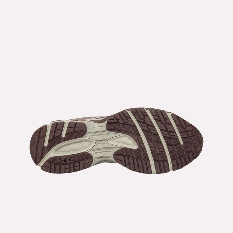 The image displays the outsole of the Reebok Premier Road Modern LTD Shoes, featuring a predominantly brown color with beige accents and a visible Reebok logo positioned at the arch. The tread showcases geometric grooves for traction, embodying the innovative design associated with this model.