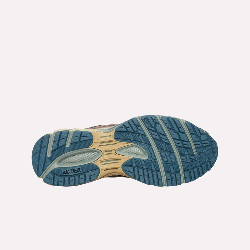 The Premier Road Ultra LTD Shoes from Reebok feature a blue and beige treaded sole with Reebok branding. The outsole showcases grooves and textured sections for superior grip, while the dual-density midsole provides enhanced comfort and support—making these sneakers perfectly suited for running. Presented against a plain light background.