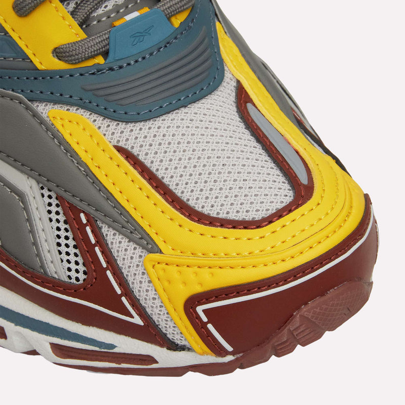 Close-up of the Reebok Premier Road Ultra LTD Shoes, featuring a white mesh base with yellow, blue, gray, and maroon leather overlays and a glimpse of the textured maroon outsole—an archival running sneaker by Reebok designed with a dual-density midsole for enhanced comfort.