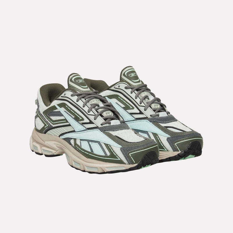 A pair of Reebok Premier Road Ultra Shoes featuring layered paneling in green, gray, and white hues sit side by side on a white background; their design showcases an archival running silhouette with lace-up fronts and thick soles equipped with a dual-density midsole.