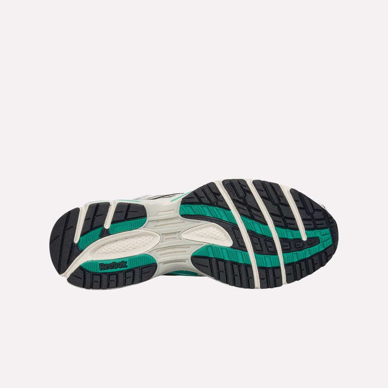 The image displays the treaded sole of the Reebok Premier Road Ultra Shoes, showcasing black, green, and cream segments with textured grips. A dual-density midsole enhances comfort and support, while the green Reebok logo near the heel area emphasizes the shoe’s archival running sneaker heritage.
