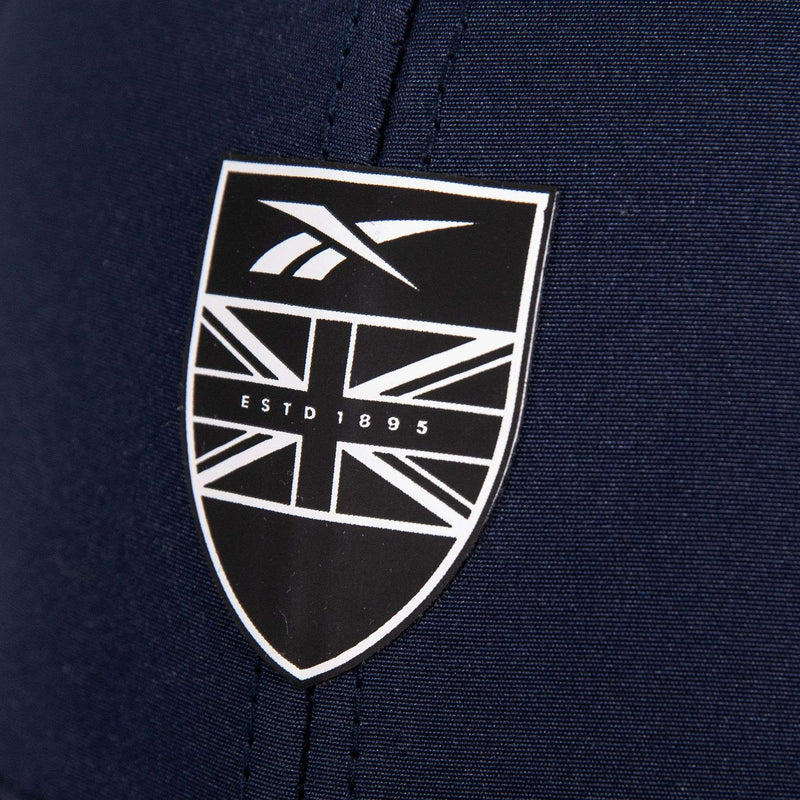A close-up of the Reebok 1895 Pro's navy fabric displays a black and white shield logo with a stylized Union Jack, the Reebok branding, and "ESTD 1895" text.