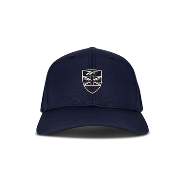 The Reebok 1895 Pro is a navy blue baseball cap with a curved brim, featuring a black and white shield emblem displaying a stylized Union Jack flag and a small logo above it on the front.