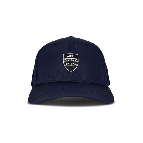 The Reebok 1895 Pro is a navy blue baseball cap with a curved brim, featuring a black and white shield emblem displaying a stylized Union Jack flag and a small logo above it on the front.