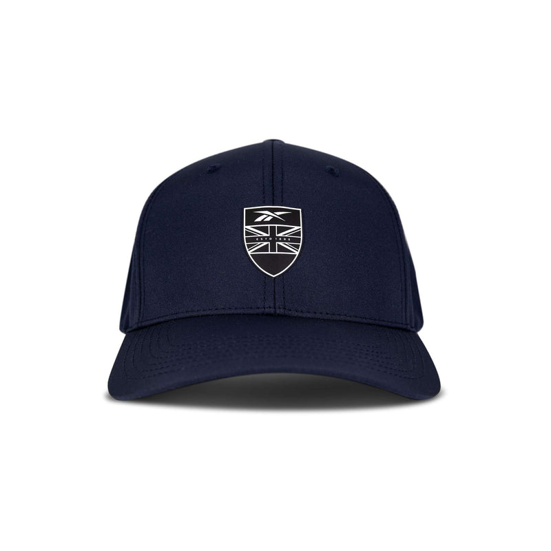 The Reebok 1895 Pro is a navy blue baseball cap with a curved brim, featuring a black and white shield emblem displaying a stylized Union Jack flag and a small logo above it on the front.