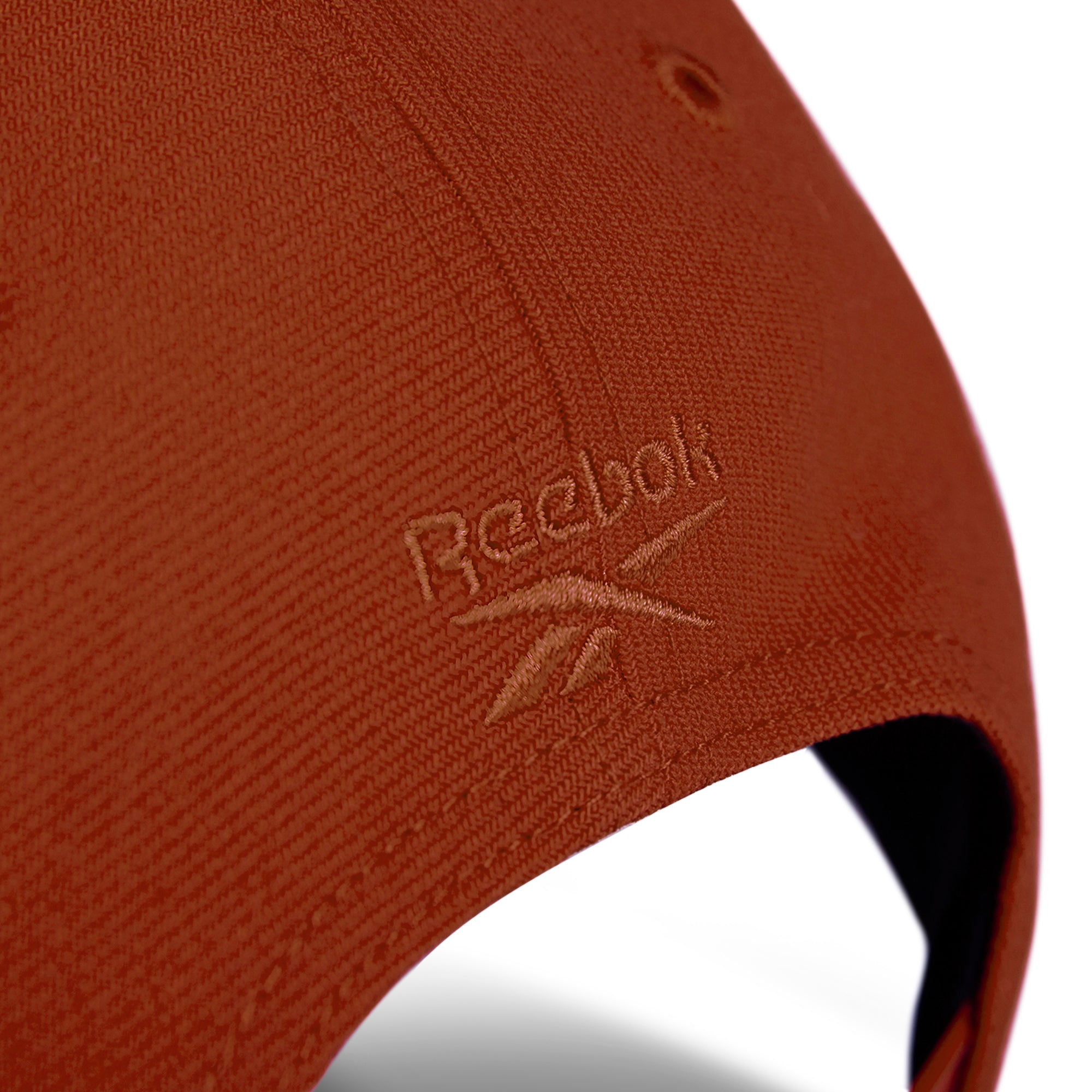 Close-up of a burnt orange Reebok Vector Baseball Cap, featuring the embroidered logo and vector symbol near its adjustable snapback closure.