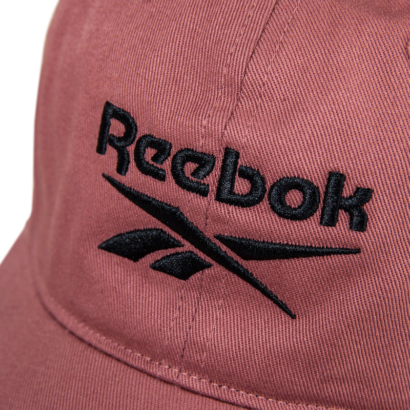 Close-up of the Reebok Logo Cap in pink cotton twill with black embroidered branding on the front and an adjustable buckle closure for comfort.