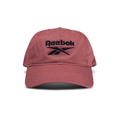 The Reebok Logo Cap is a maroon cotton twill cap with a curved brim and black embroidered logo on the front. It features an adjustable buckle closure and is shown against a white background.