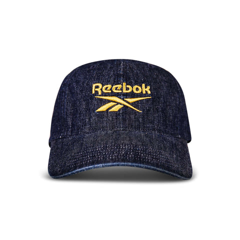 The Reebok Denim Logo Cap features dark denim, a curved brim, and the yellow Reebok logo and name embroidered on the front, displayed against a white background.