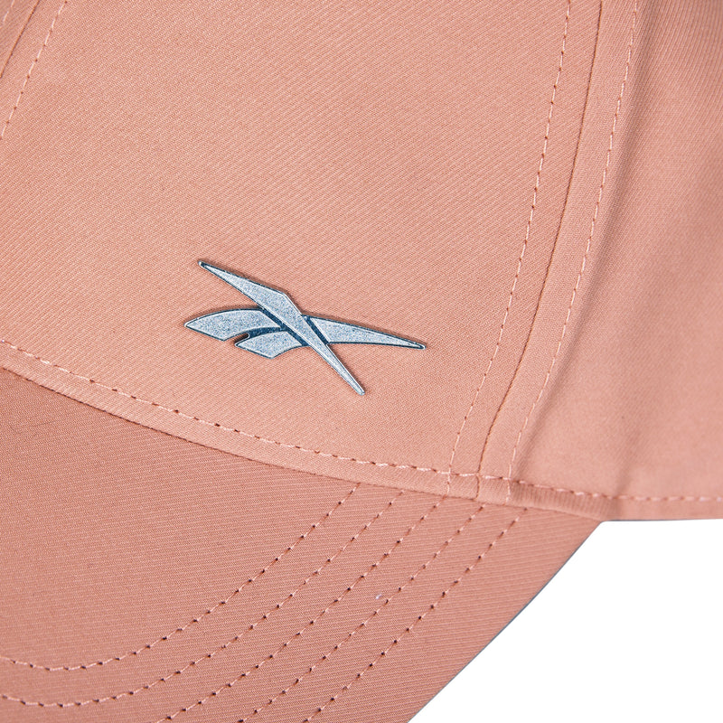 Close-up of a peach Reebok Badge Cap with moisture-wicking fabric, visible stitching, and a silver Reebok logo on the front panel.