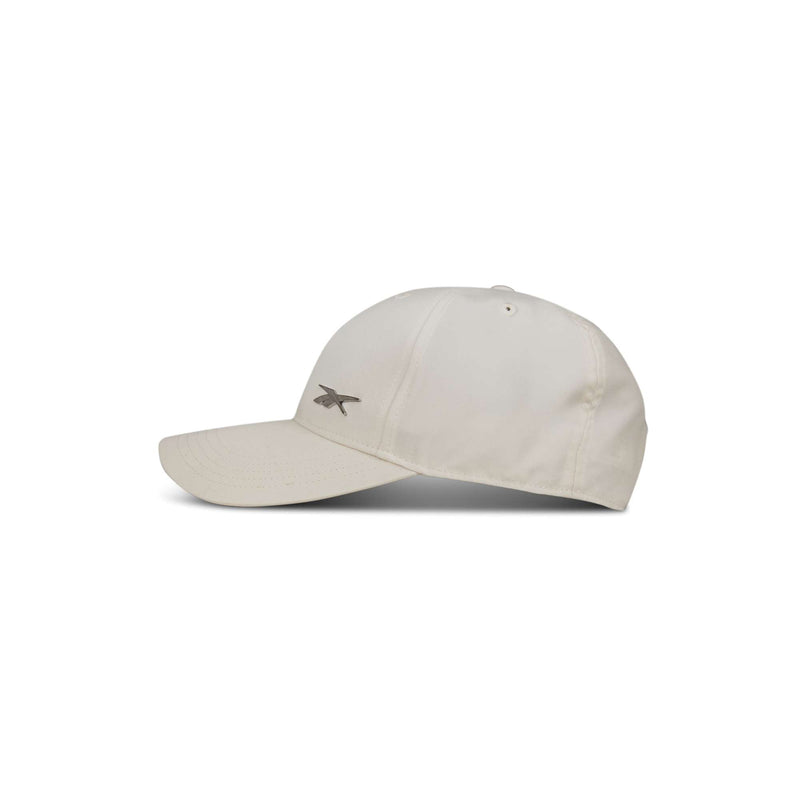 The Reebok Badge Cap in beige features a curved brim and a small gray logo on the front left panel, displayed against a white background.
