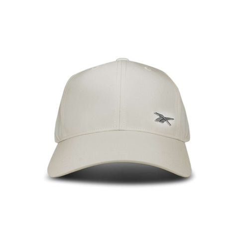The Reebok Badge Cap is a beige baseball cap featuring a small silver embroidered logo on the front left side, shown against a white background.