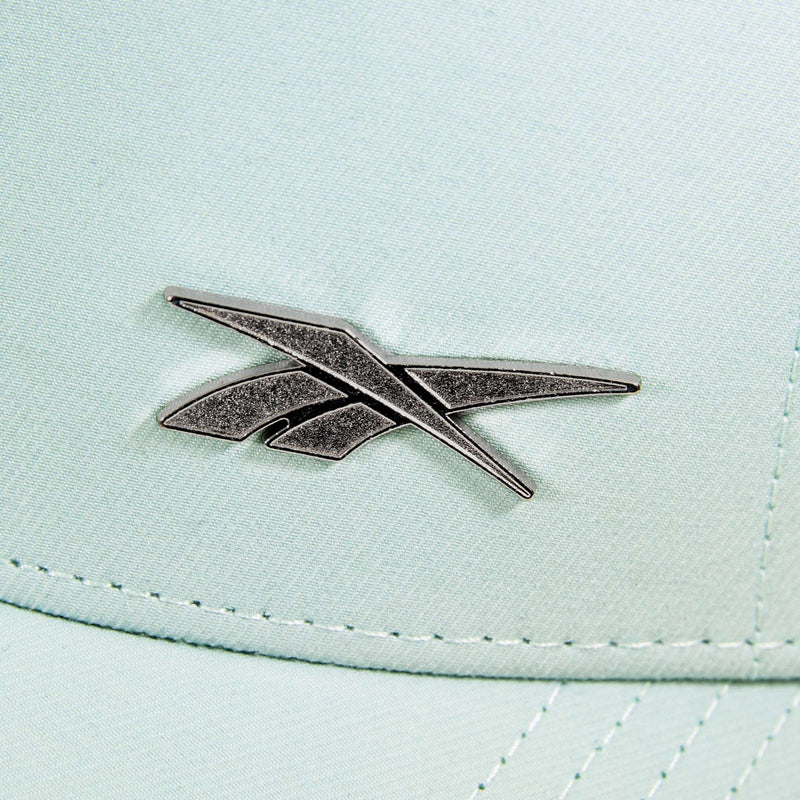 Close-up of a silver Reebok logo emblem on light mint green fabric, showing detailed stitching on the Reebok Badge Cap, which features a moisture-wicking Speedwick sweatband for comfort.