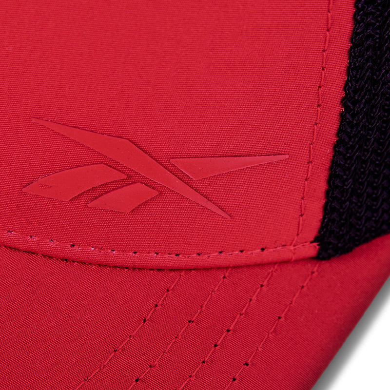 Close-up of the red Reebok Athlete Cap featuring an embossed Reebok logo on the front, black mesh fabric on the side, and detailed stitching along the seam.