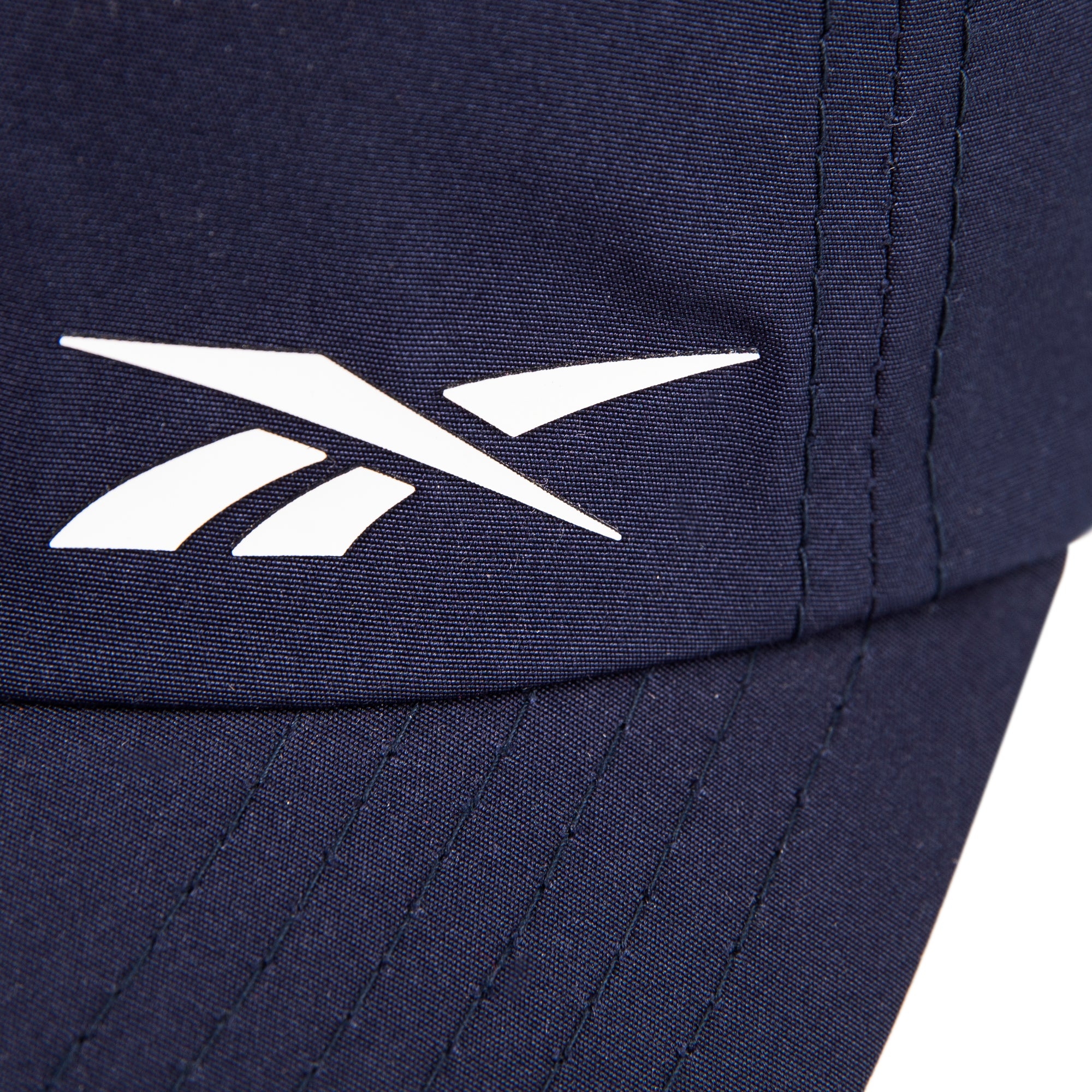 Close-up of the Reebok Flow Cap in navy blue, made from recycled polyester. Features a white Reebok logo near the stitched seam and a moisture-wicking sweatband for comfort.