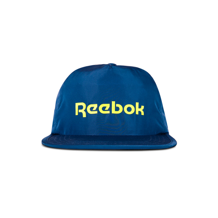 The Reebok Flat Brim Running Cap is a blue, lightweight hat with moisture-wicking fabric, featuring a flat brim and bold yellow Reebok logo on the front, shown against a white background.